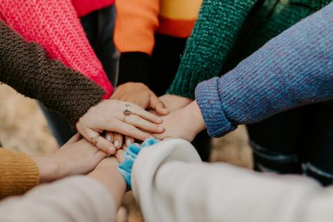 close up shot of a group of women standing in a circle, hands reaching out to the center, placed upon each other.